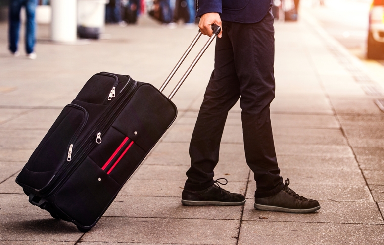 Unrecognizable businessman with luggage waiting at the airport, going to enter a bus, sunny day