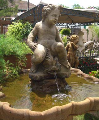 Classical stone putti sitting on a dolphin spouting water fountain